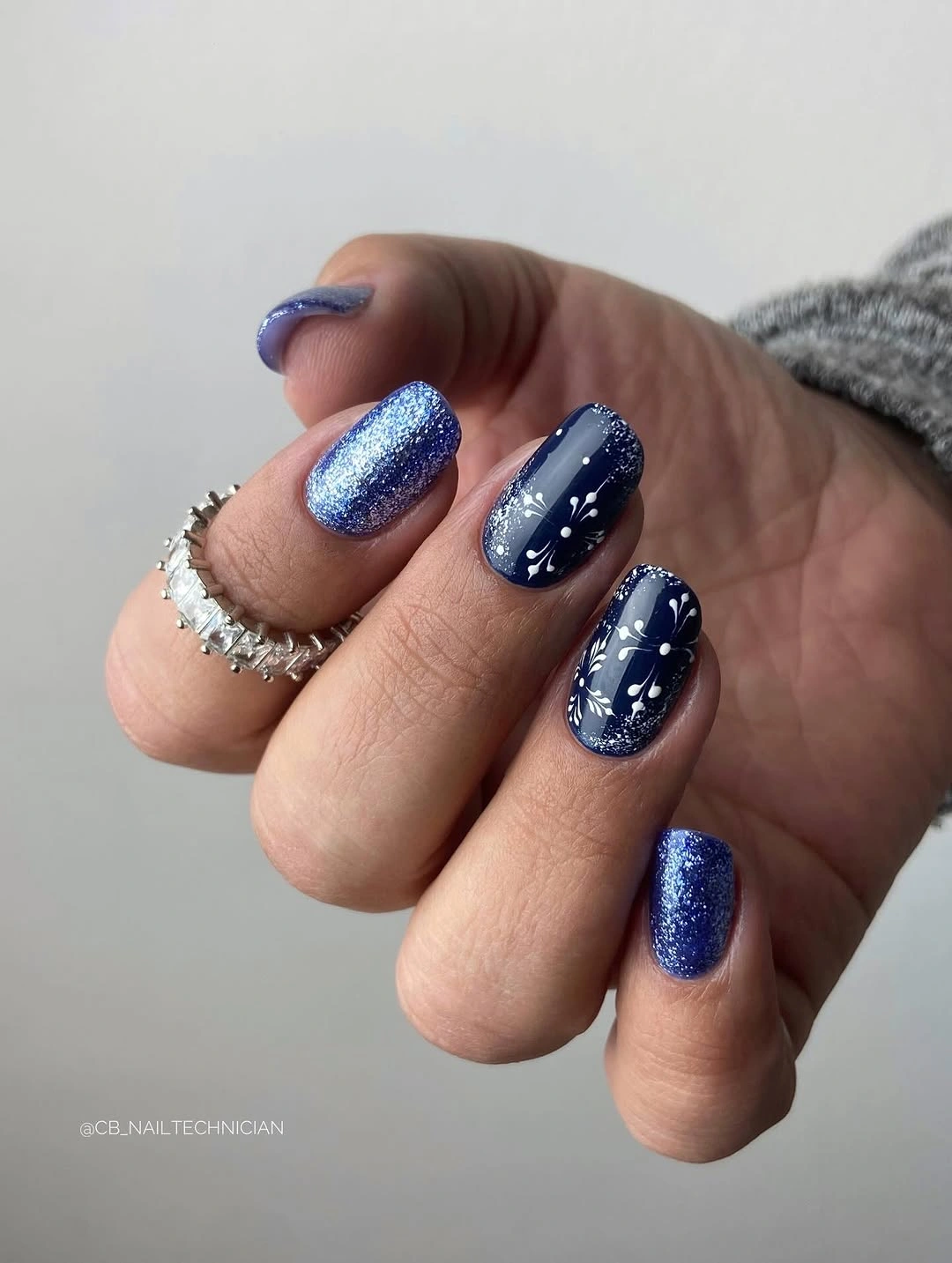 Blue glitter nails with navy polish and white starburst accents