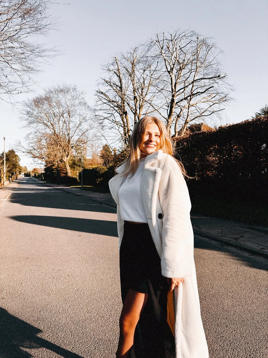 White coat, black skirt outfit and black boots outdoors