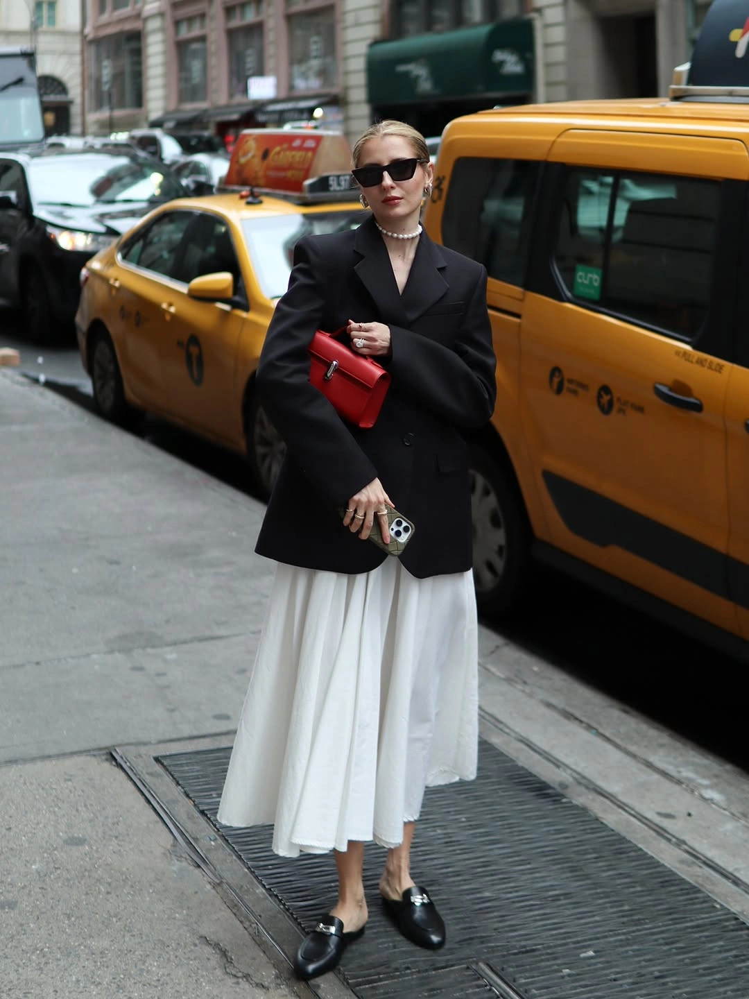 Black blazer, white pleated skirt, loafers and red handbag