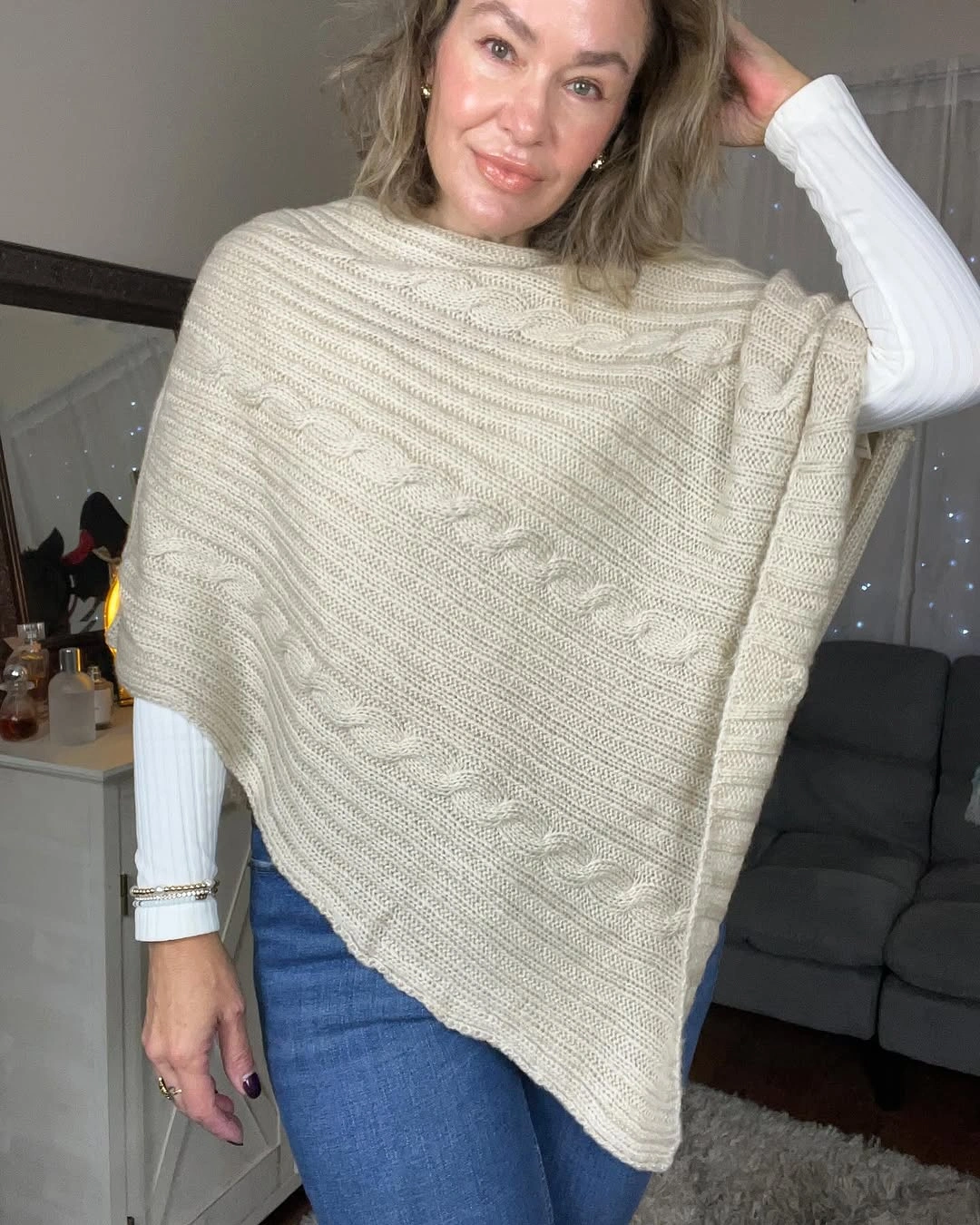 Cream cape-like knit layer over white top and jeans