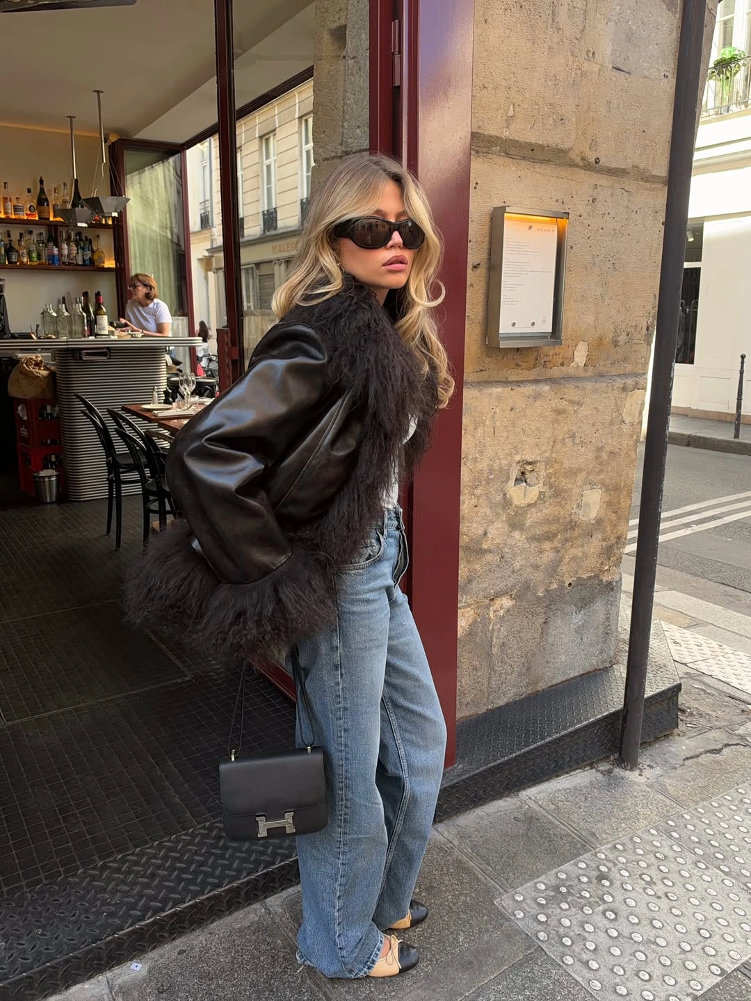 Woman wearing black textured leather-look jacket, light blue jeans and dark sunglasses