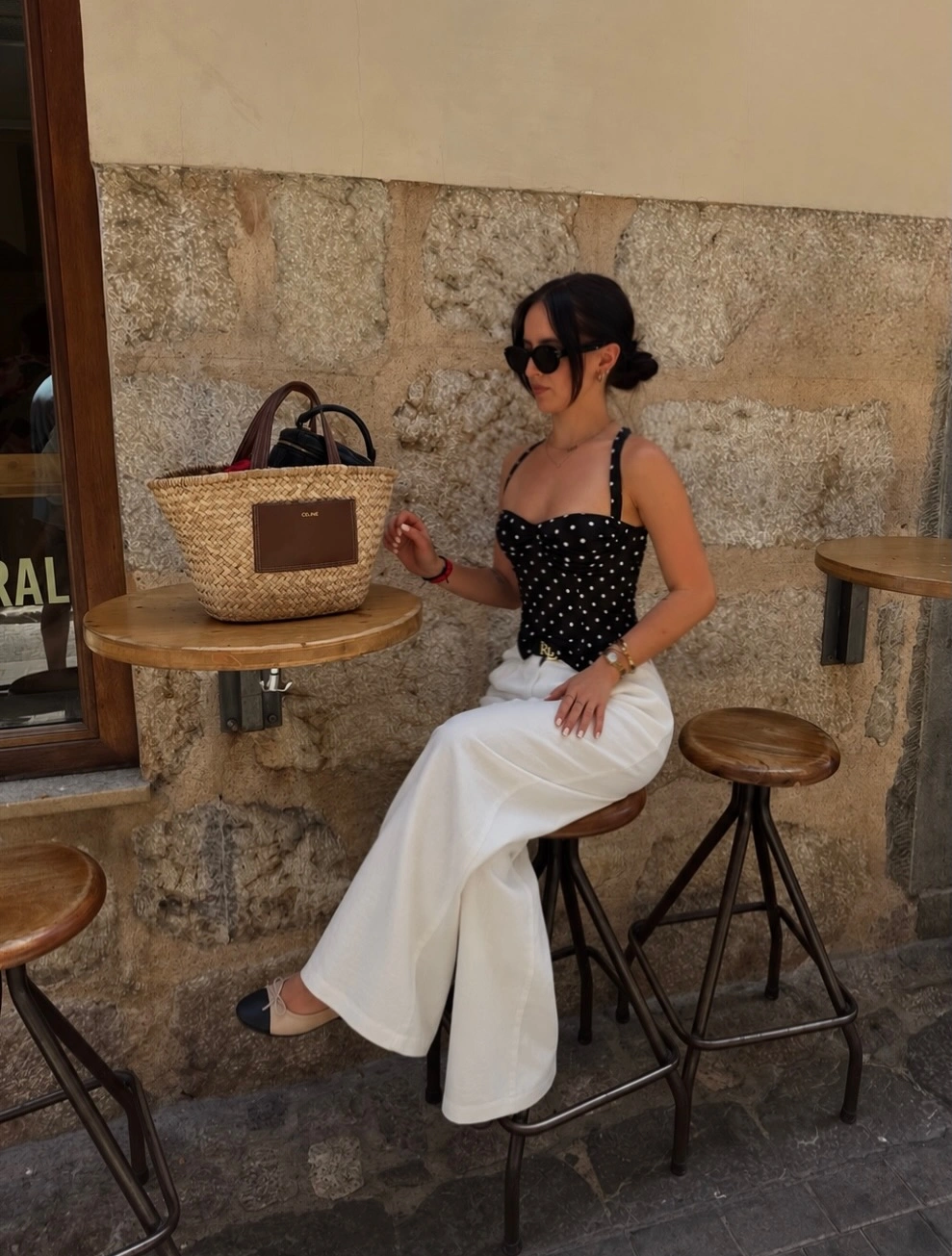 Black polka-dot strappy top with flowing white trousers and woven handbag
