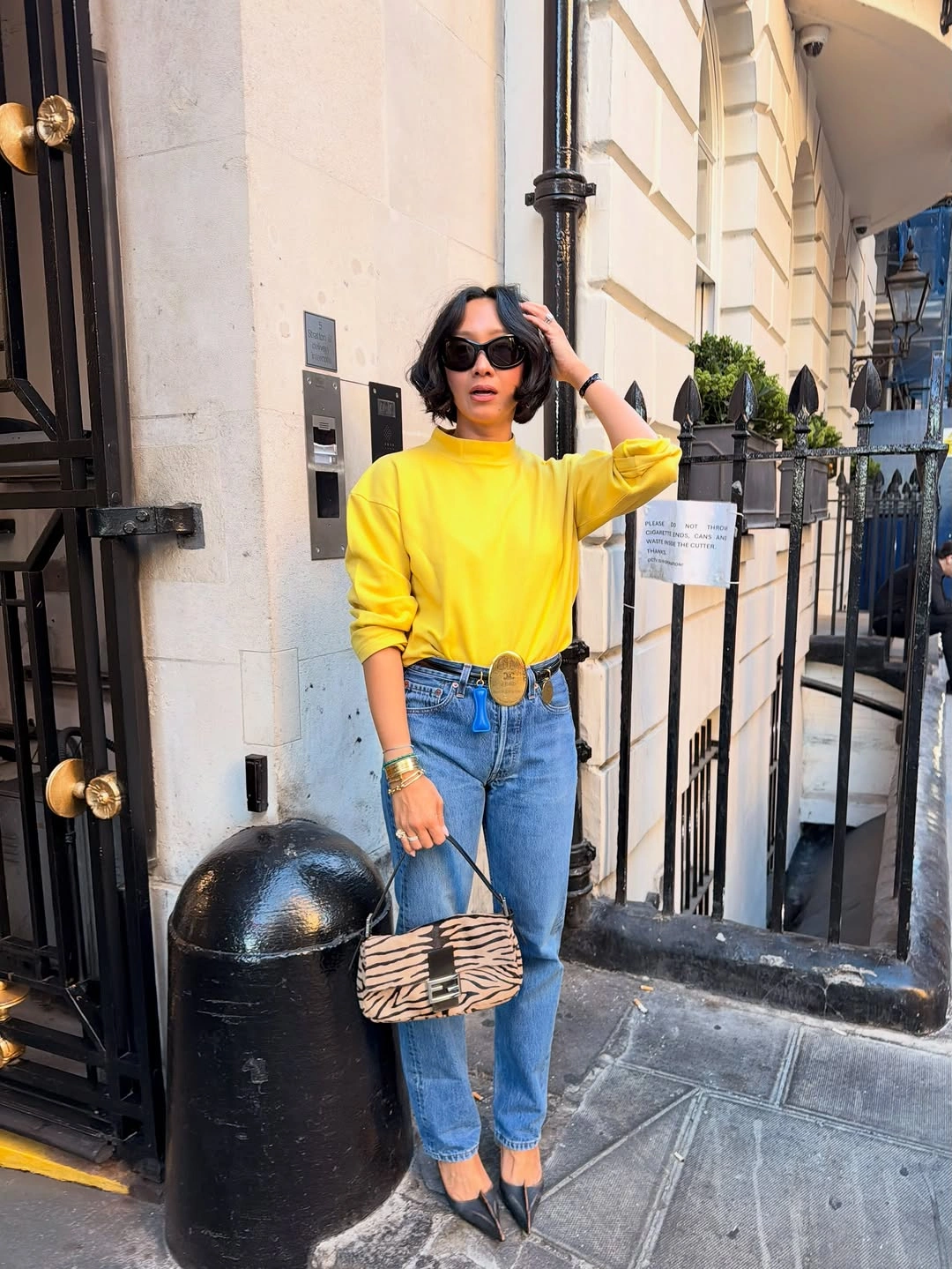 Bright yellow sweatshirt with blue jeans, decorative belt, pointed heels and patterned handbag