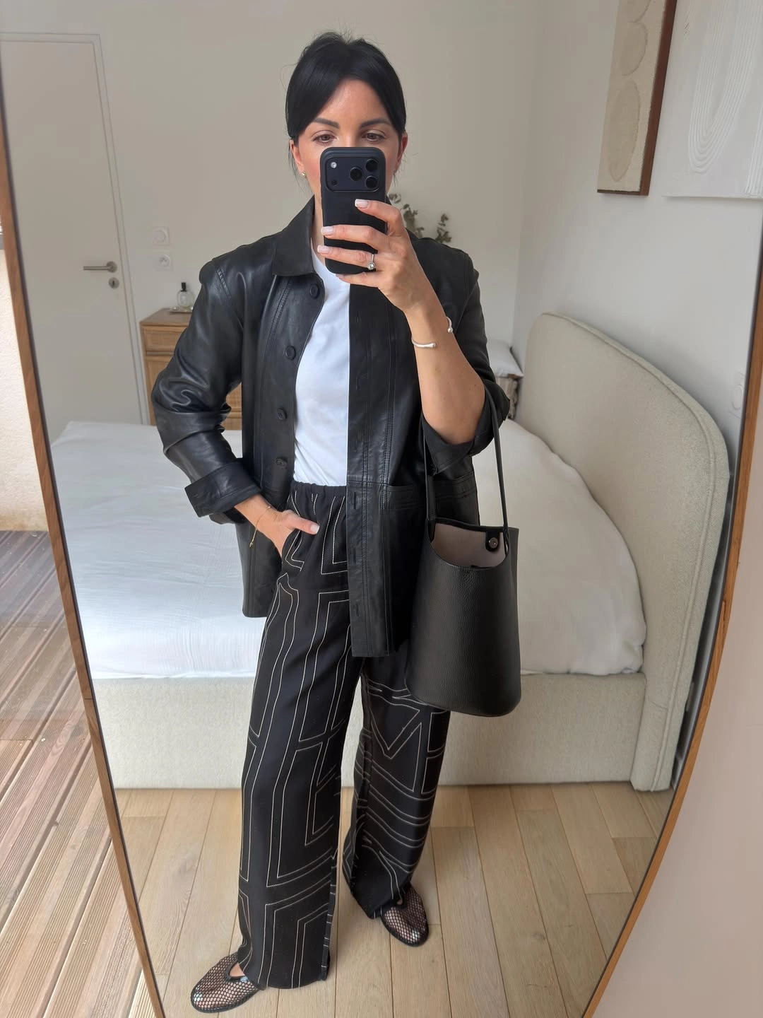 Black leather-look jacket with white top and patterned black wide-leg trousers
