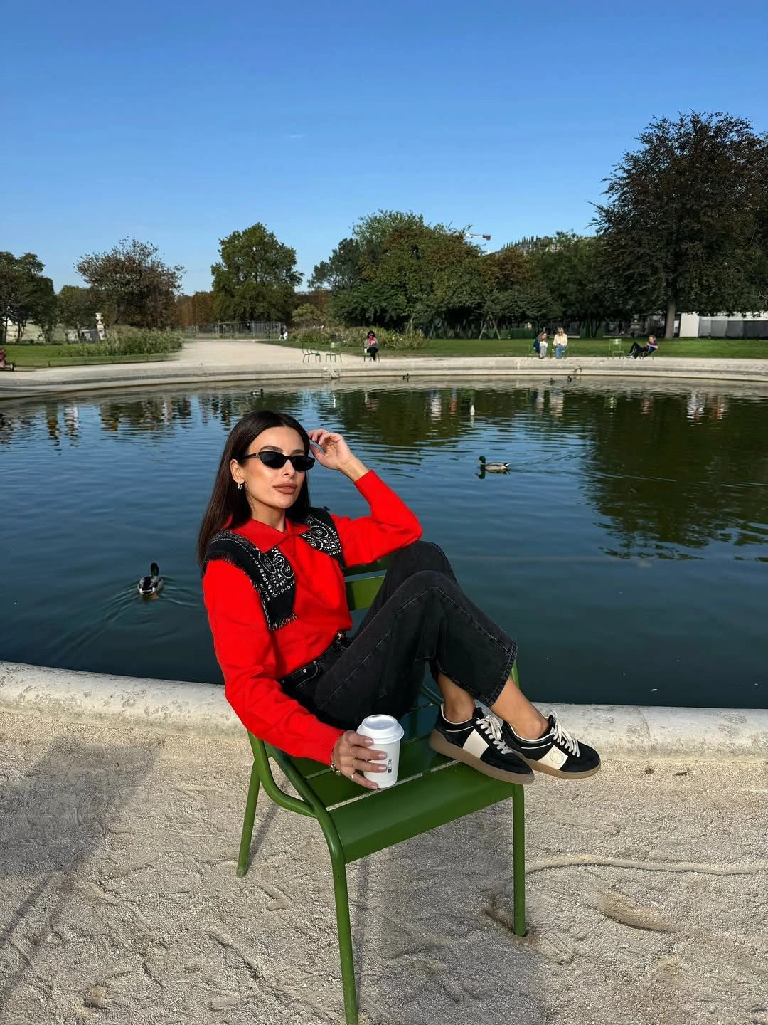 Woman in red top, black patterned vest, cropped dark jeans and sneakers