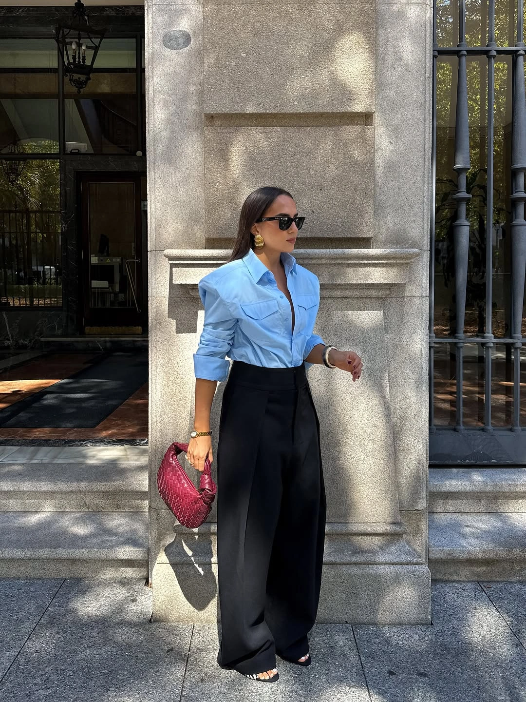 Light blue collared shirt tucked into wide black trousers with red handbag