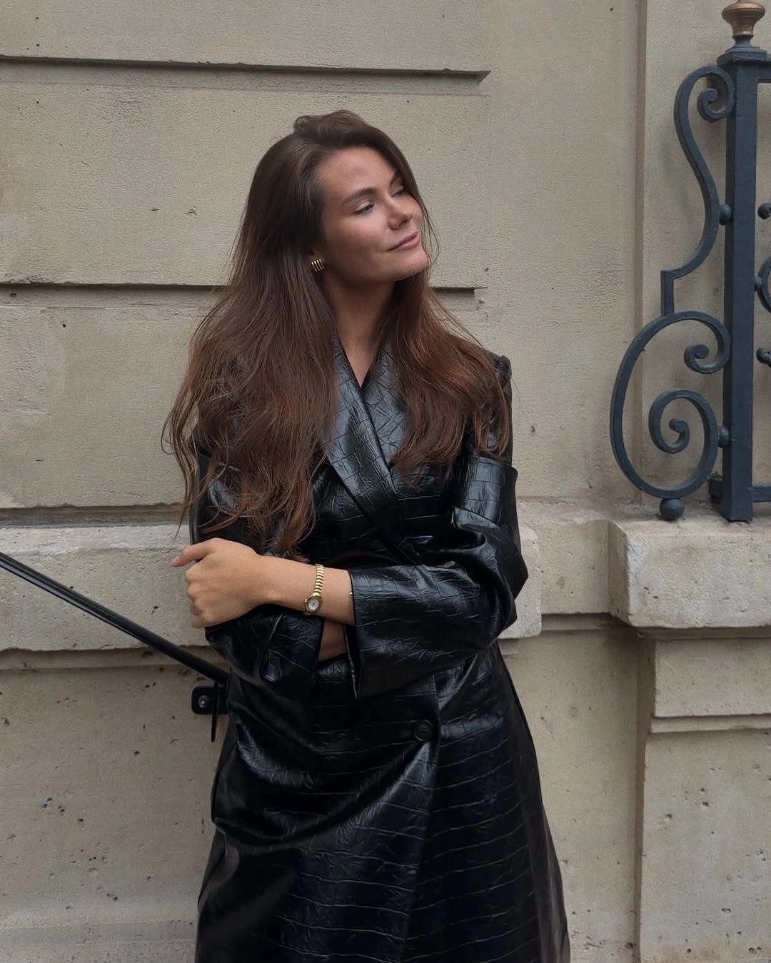 Woman wearing glossy black leather-look outfit with overlapping panels and defined waist
