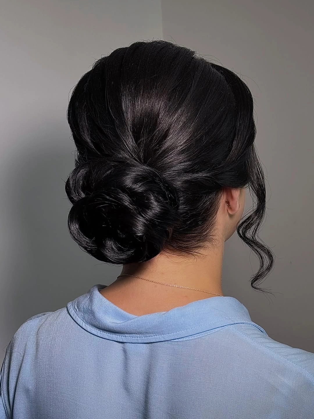 Glossy dark low bun with curled face-framing strand