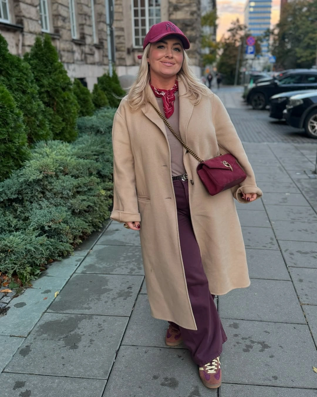 Camel long coat with burgundy trousers cap scarf bag and sneakers