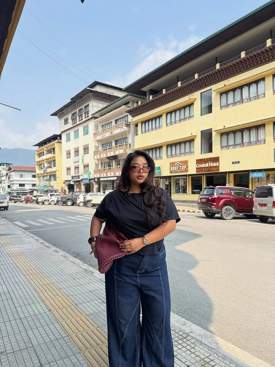 Black short sleeve top with wide blue jeans and burgundy textured clutch