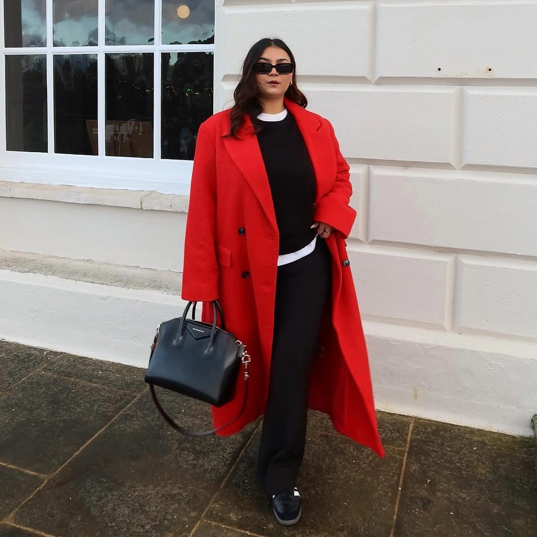 Bright red double breasted coat over black separates with handbag and sneakers