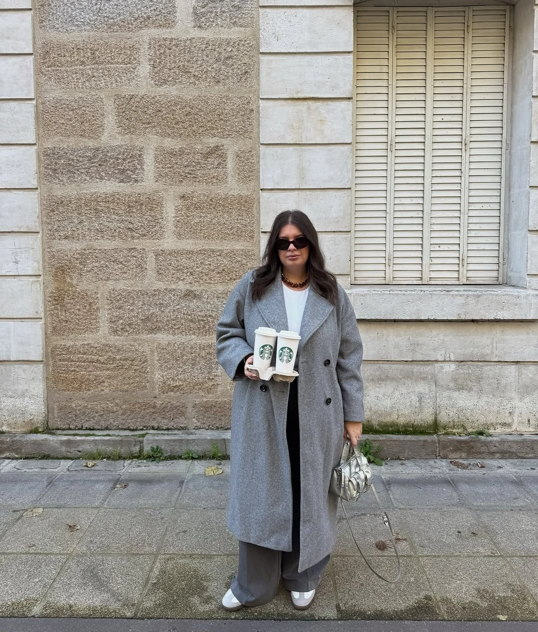Long gray coat with wide gray trousers white sneakers and silver handbag