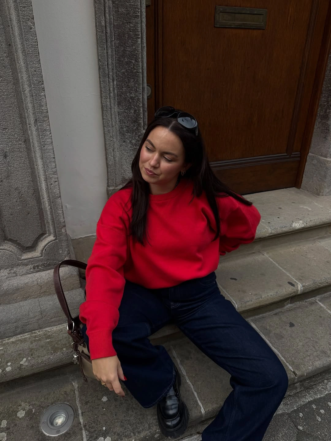 Red sweatshirt-style top with dark wide-leg jeans and loafers