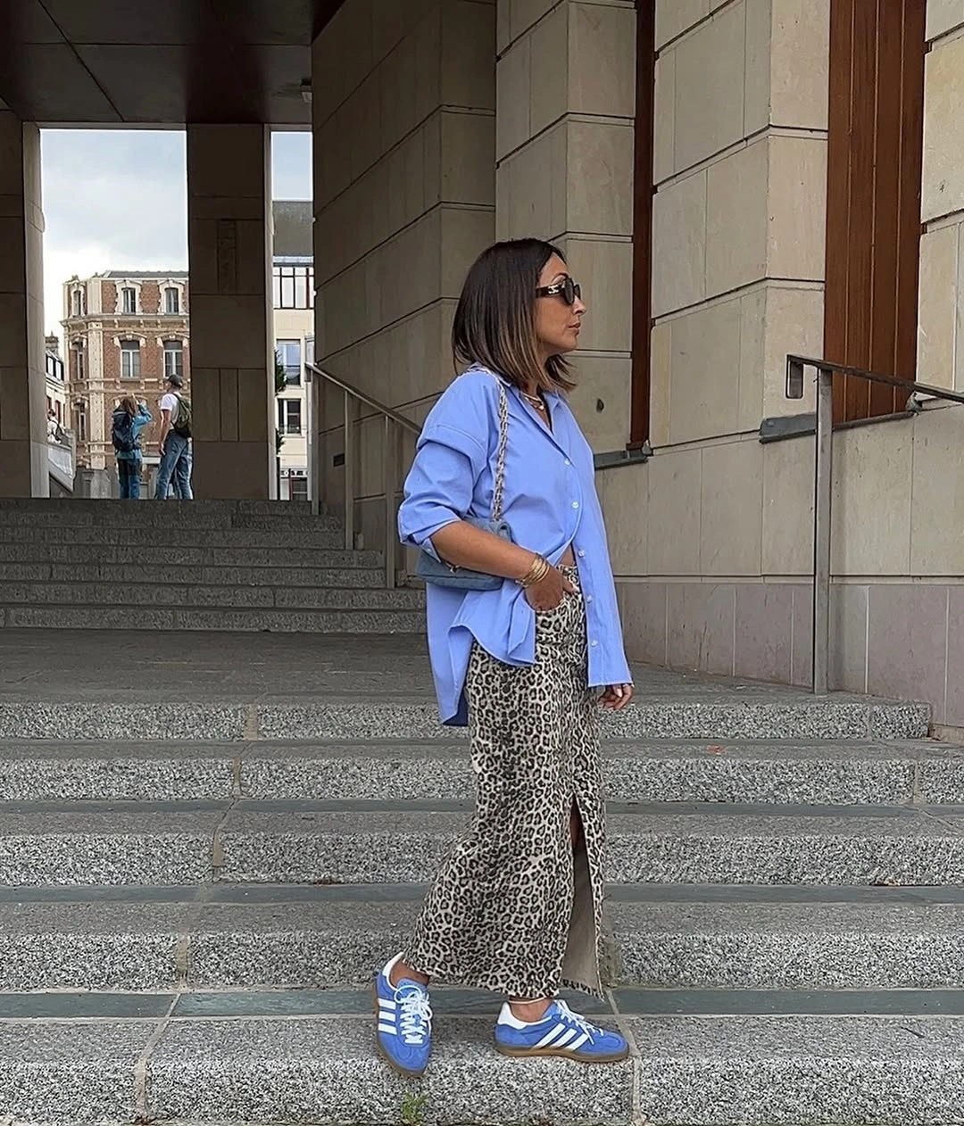 Blue oversized shirt, leopard-print trousers, blue sneakers, small chain bag