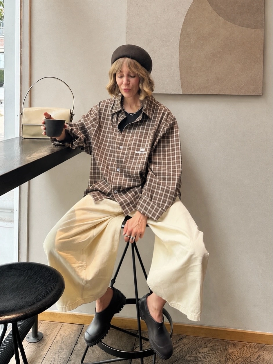 Brown checked shirt, wide cream trousers, black clogs, dark beret