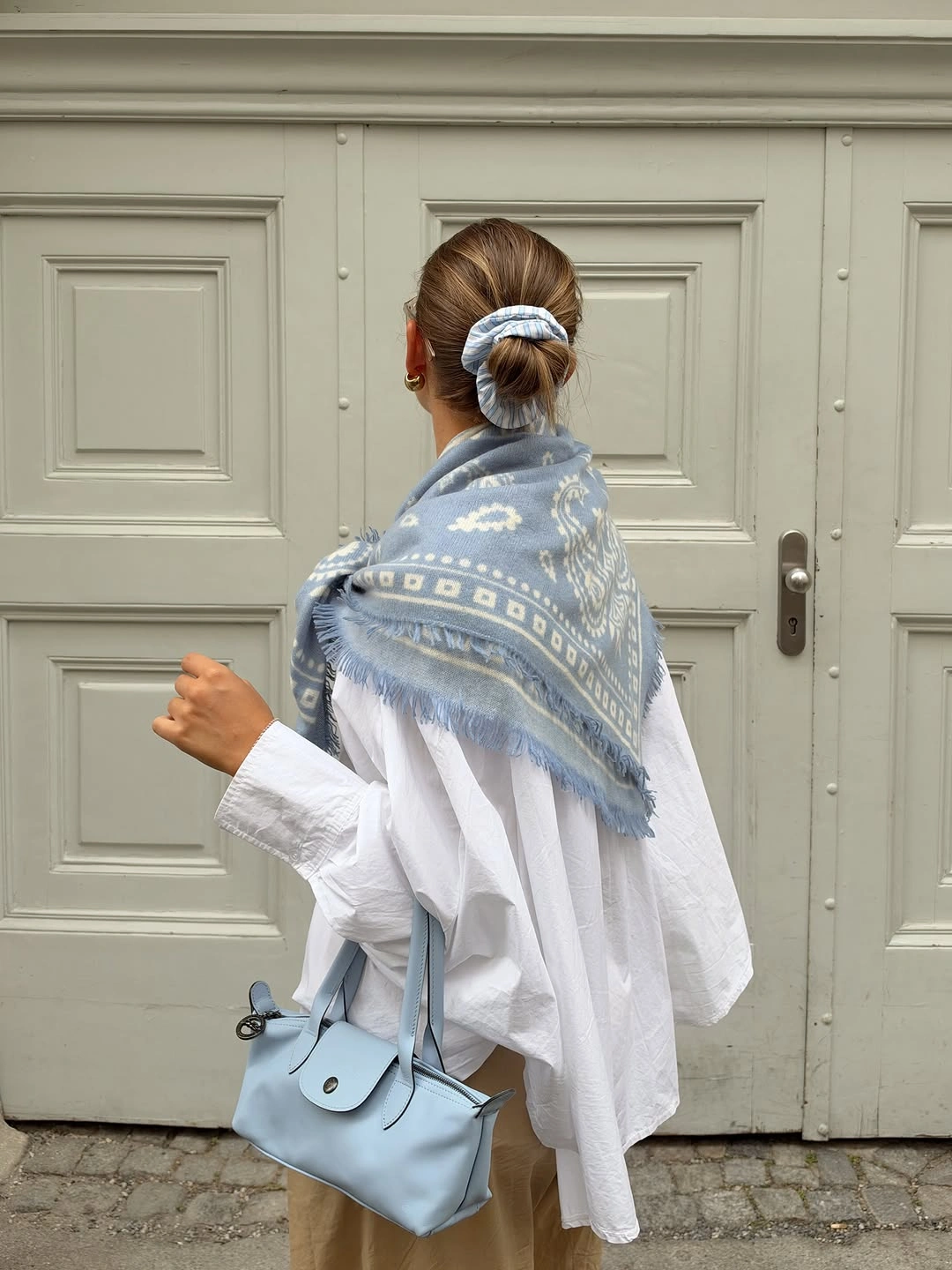 White oversized shirt, blue shawl, pale blue bag, tan trousers