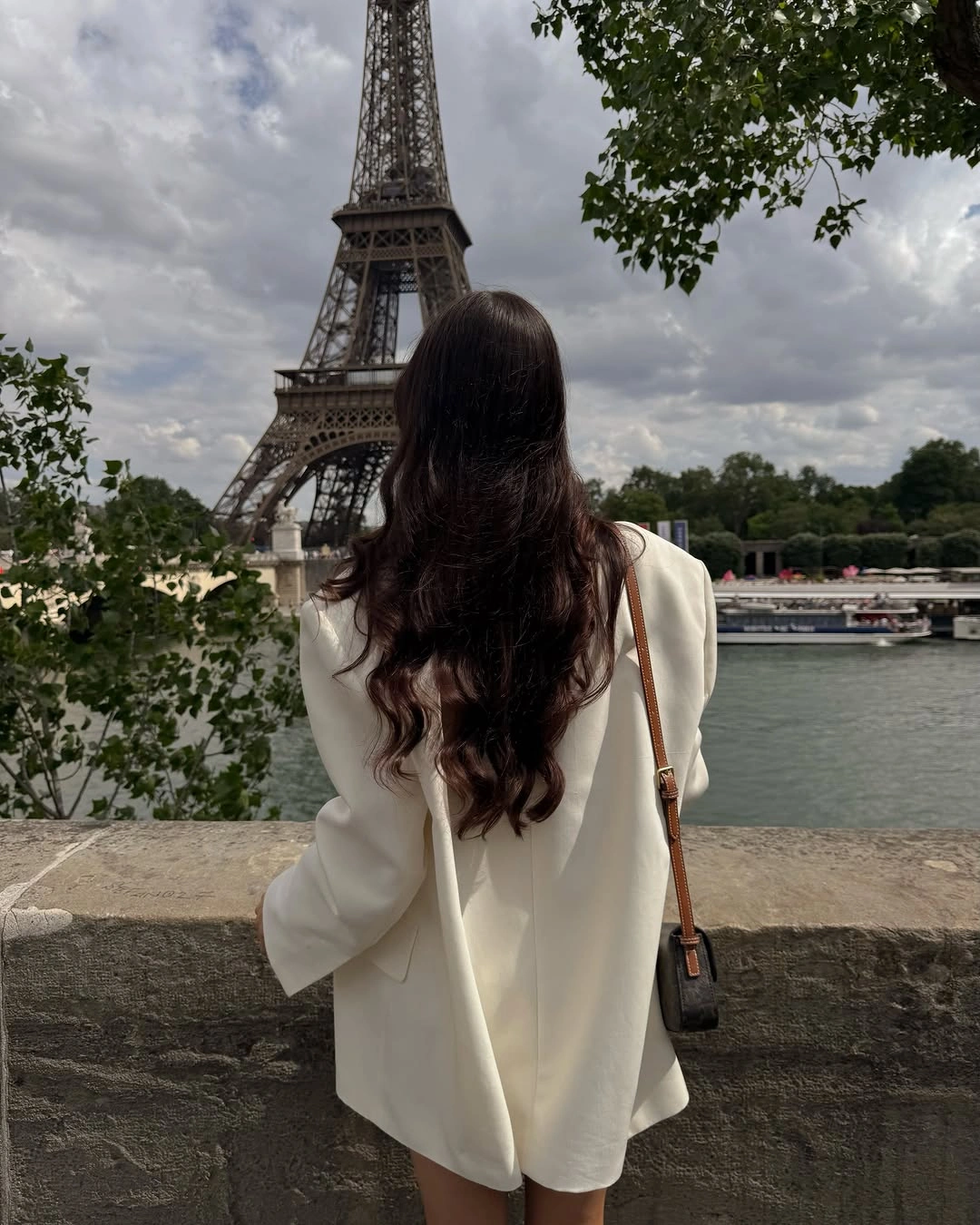 Long white blazer and dark shoulder bag overlooking the Eiffel Tower