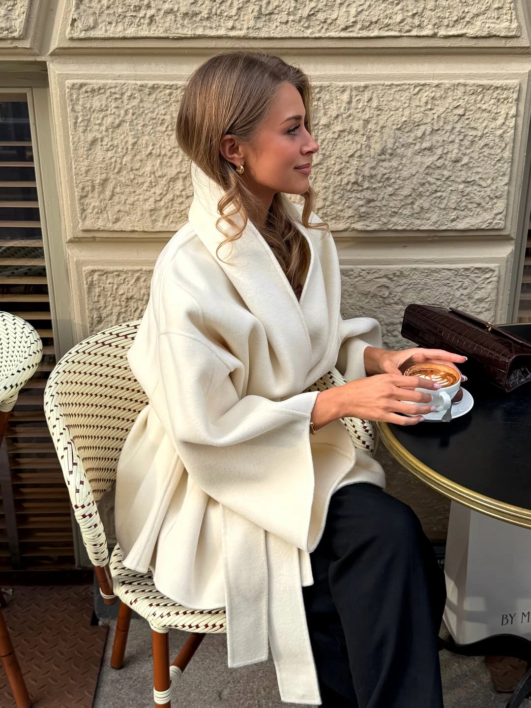 Voluminous white wrap layer, black trousers, dark brown structured bag