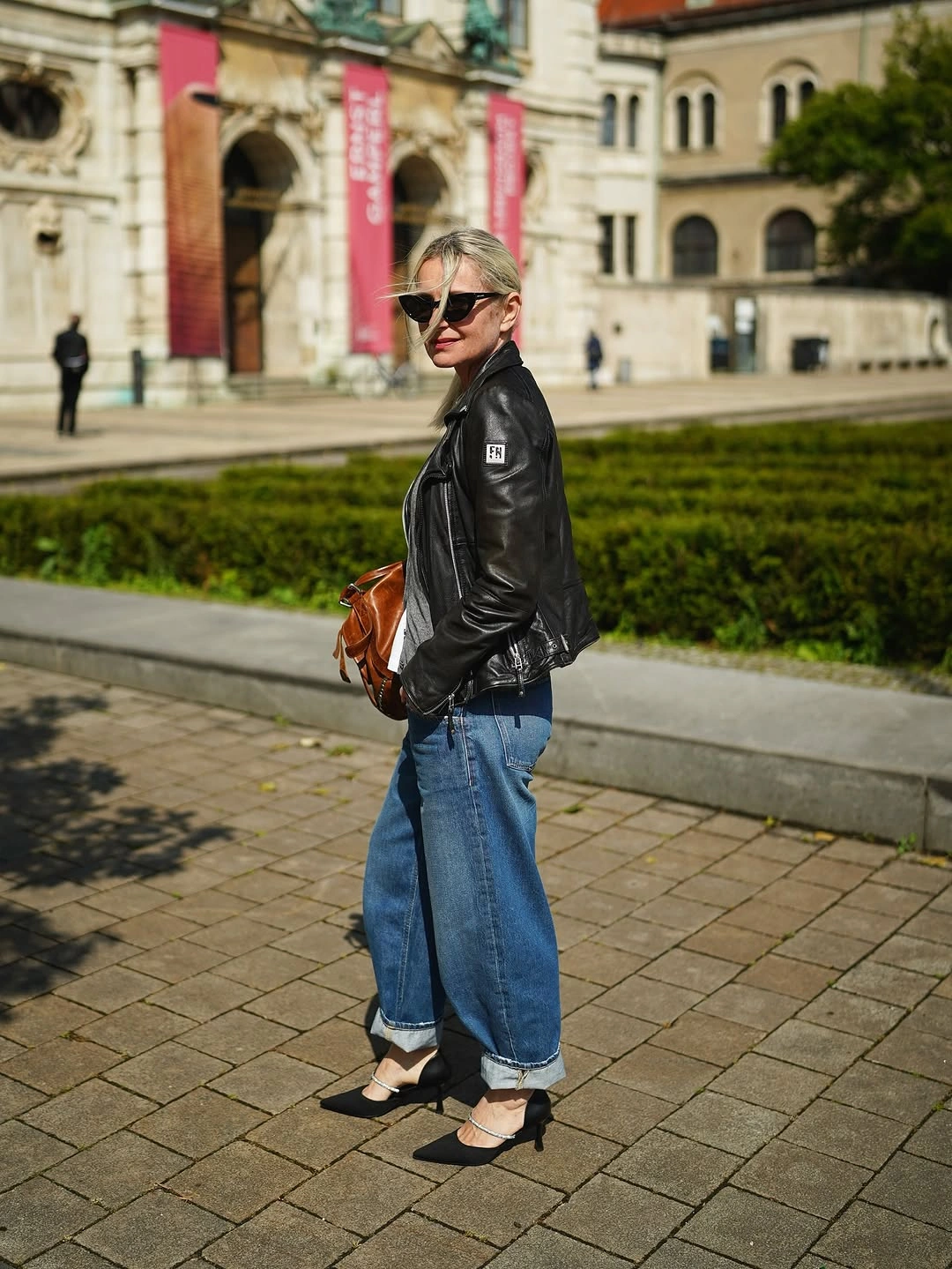 Woman in leather jacket, cropped blue jeans, socks, and strap shoes