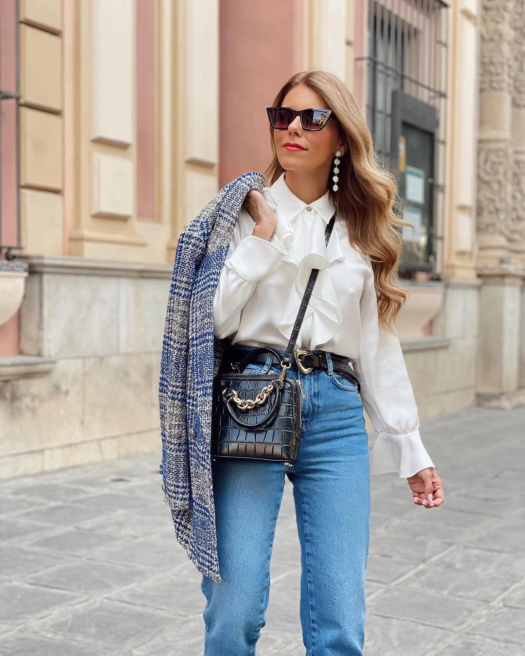 Woman in blue jeans, white ruffled blouse, and black bag