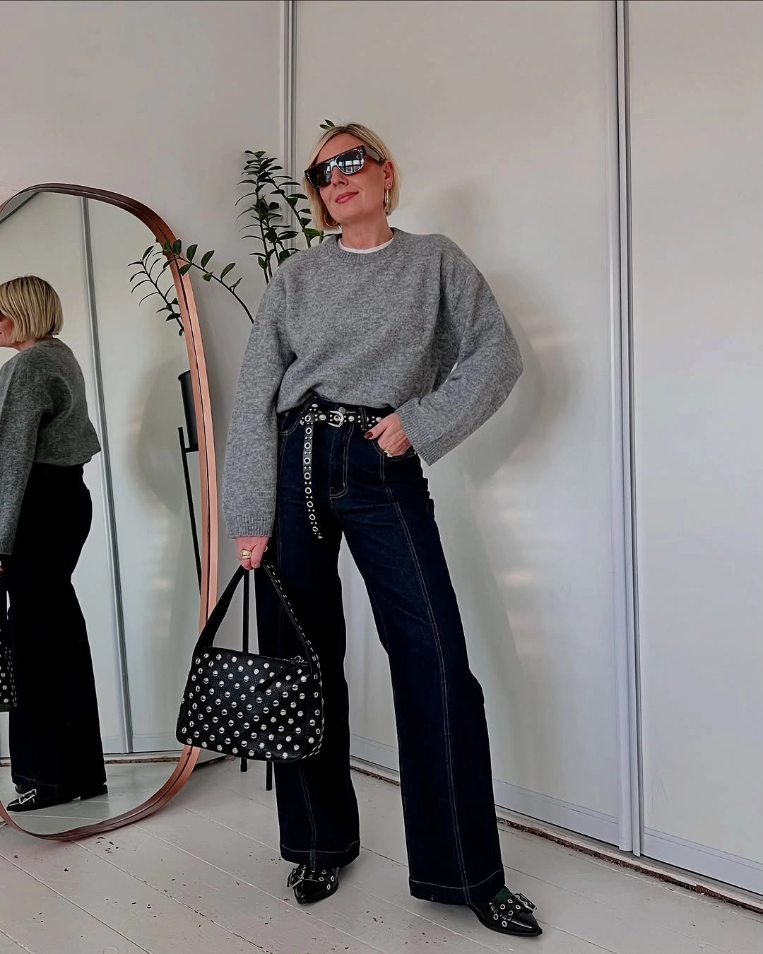 Woman in dark wide-leg jeans, gray sweater, and studded accessories