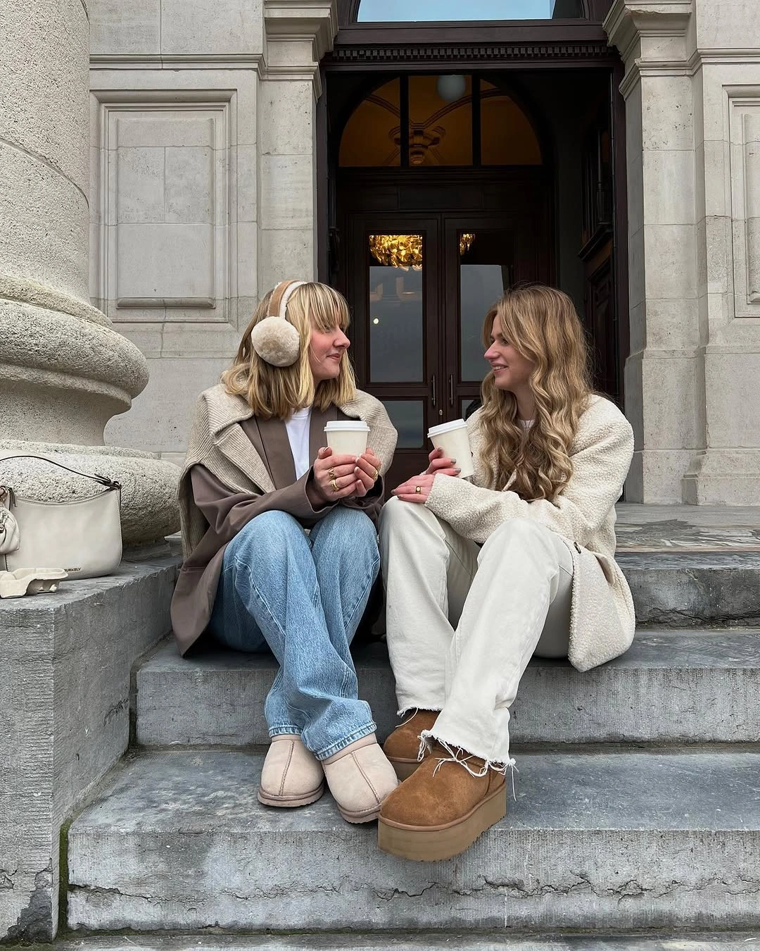 Two women in neutral layers, one wearing wide light-blue jeans