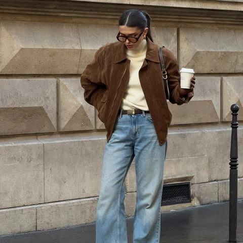 Woman in light-wash jeans, cream turtleneck, and brown jacket