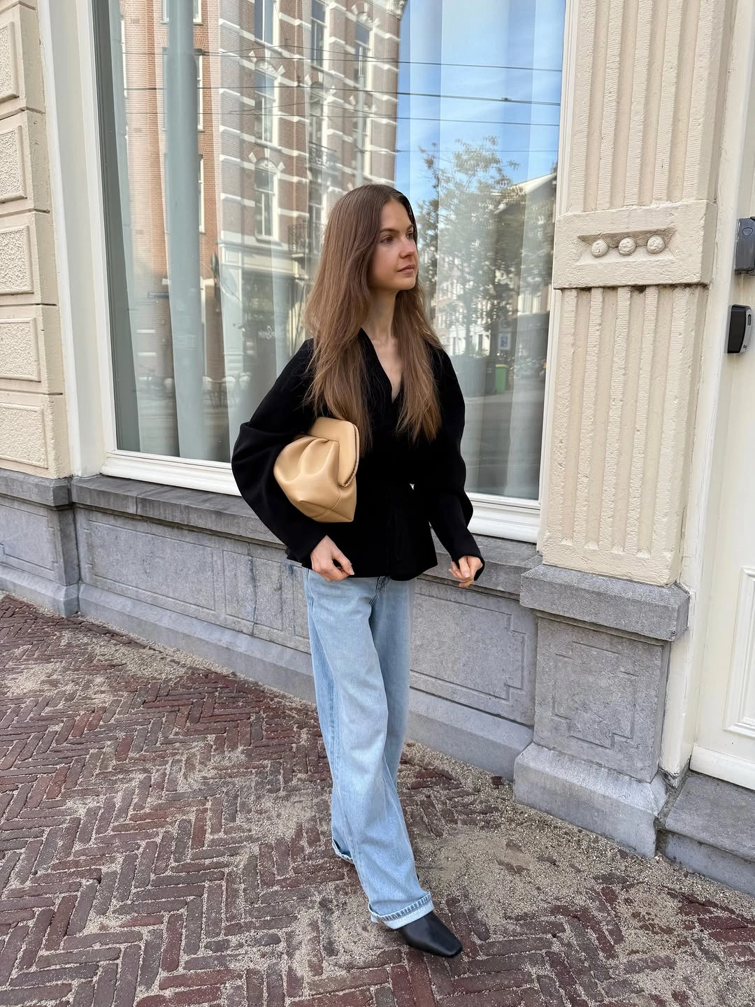 Woman in light-wash jeans, black blouse, and pointed shoes
