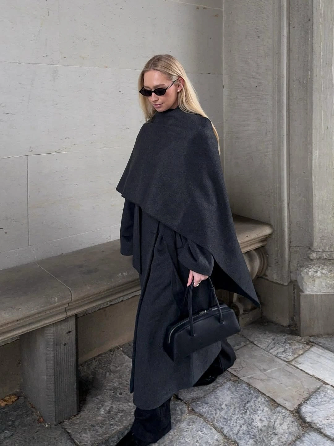 Dark charcoal asymmetric draped outfit with structured black handbag and sunglasses