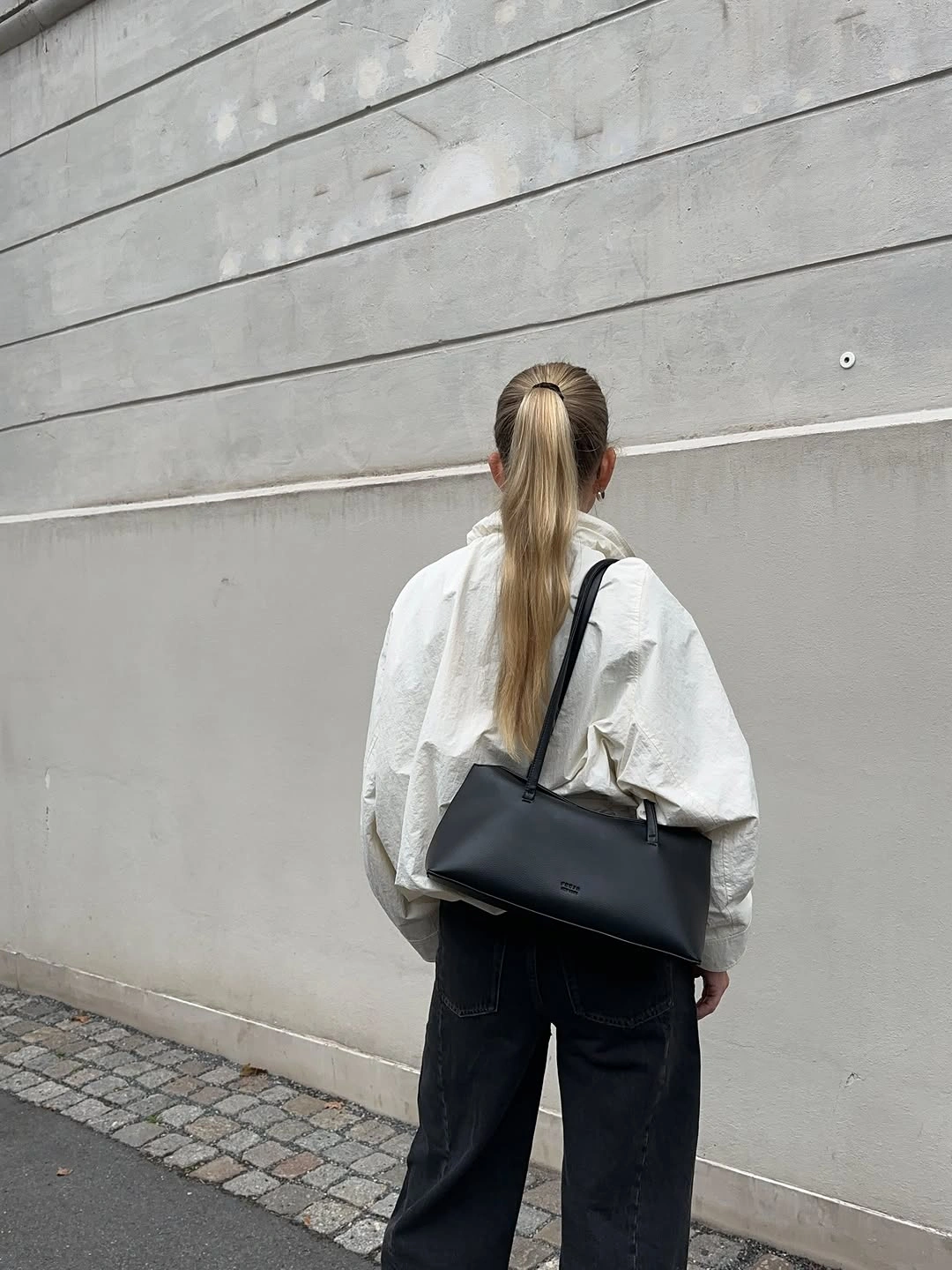 Rear view of pale oversized jacket, dark jeans, and black shoulder bag