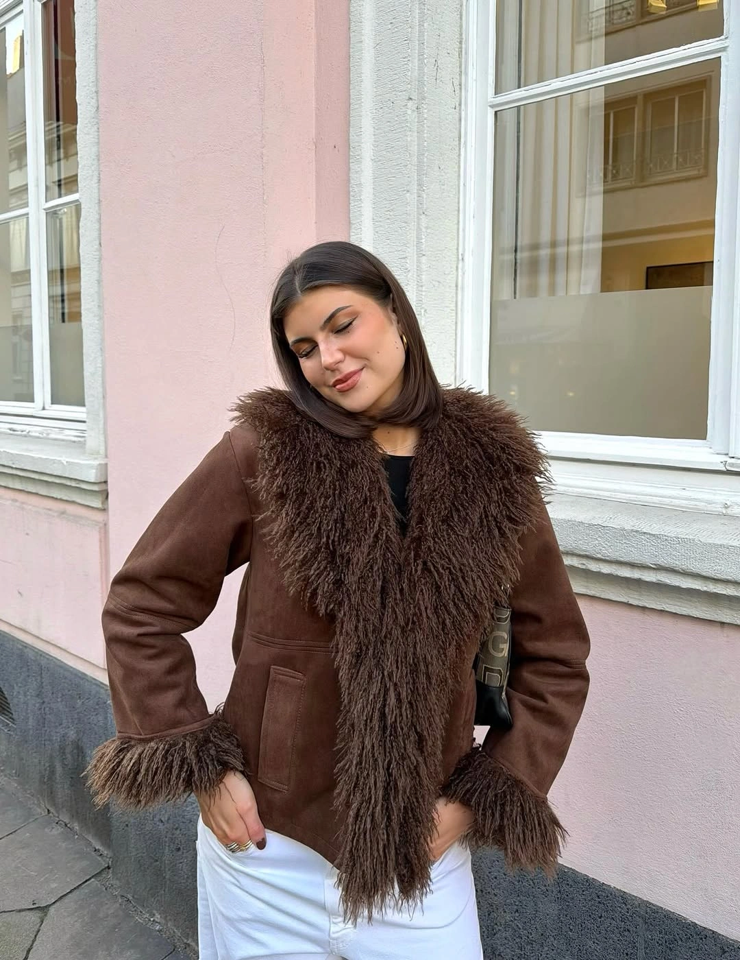 Brown jacket with shaggy trim, black top, and white trousers