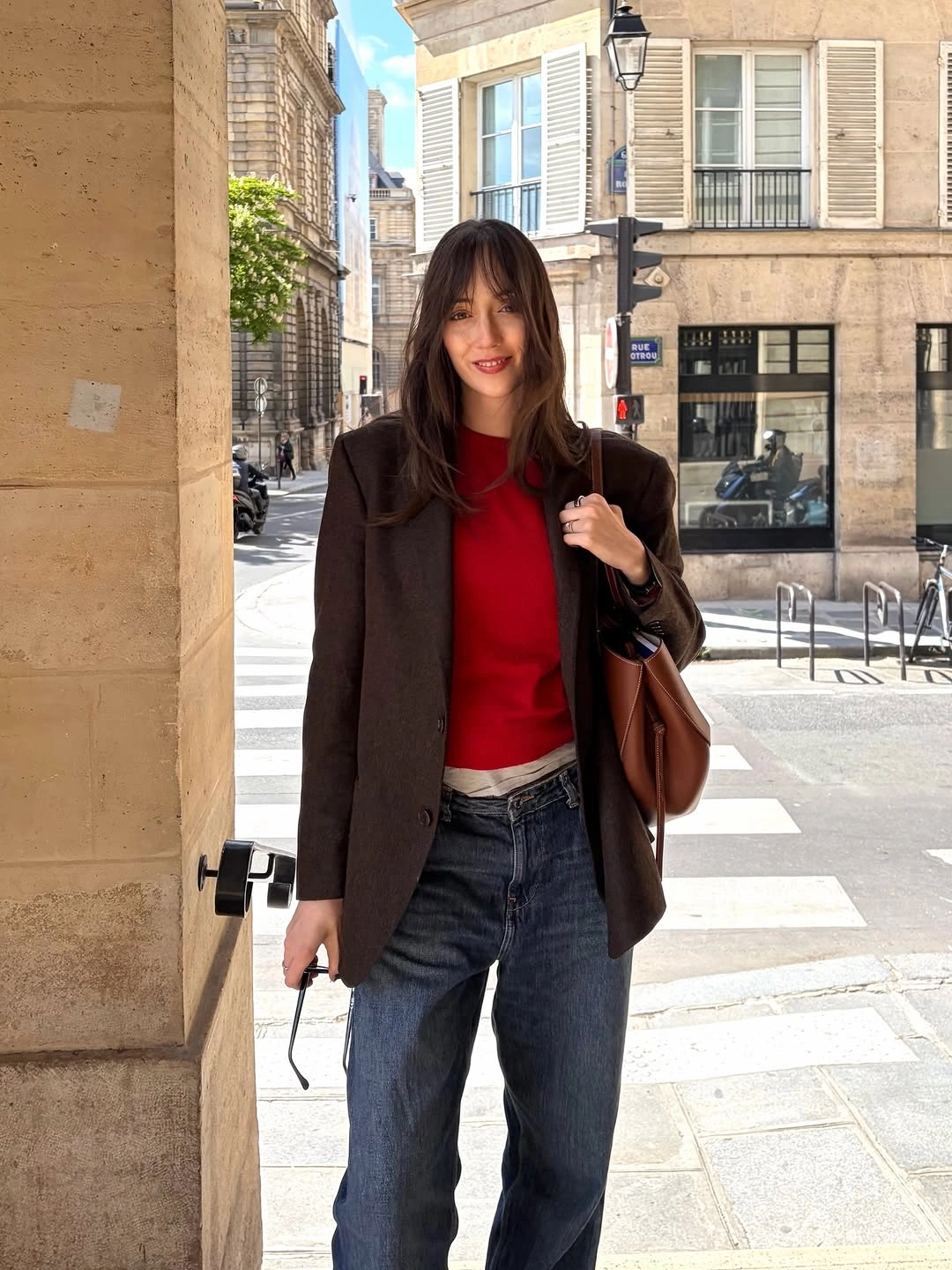 Dark brown blazer over red top with blue jeans and shoulder bag