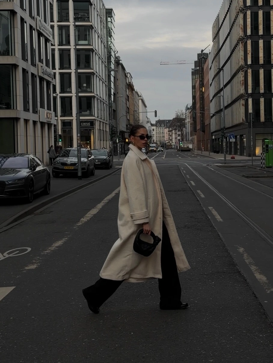 Long beige coat and pale scarf over black wide trousers