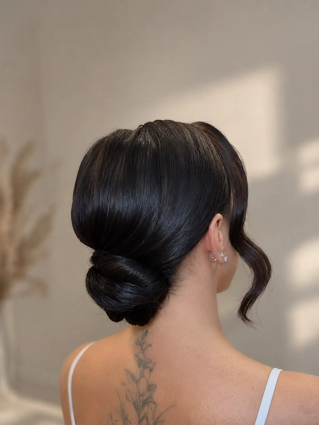 Glossy dark low bun with one curled face-framing strand