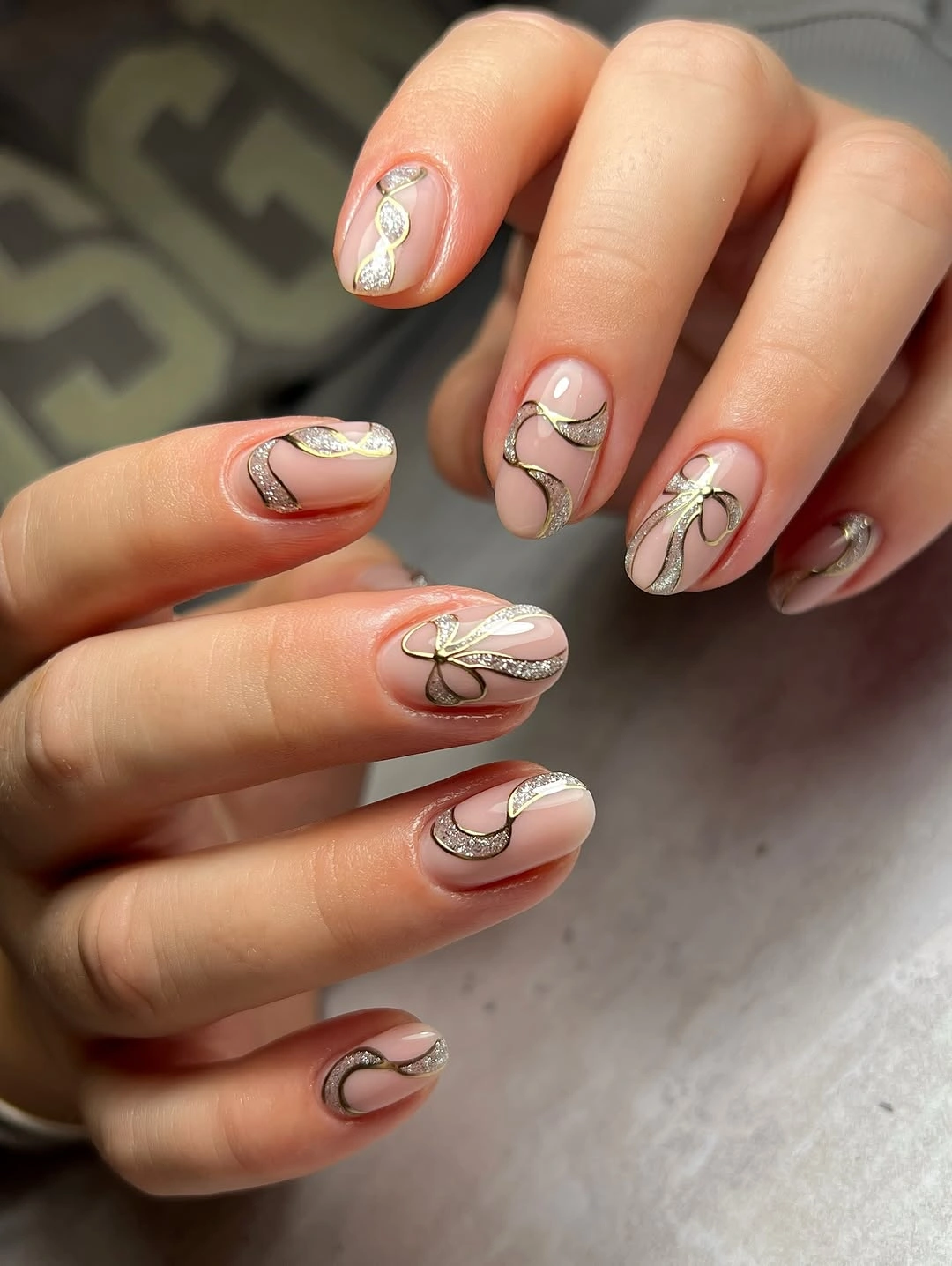 Short nude pink nails with curved silver glitter ribbons and metallic outlines