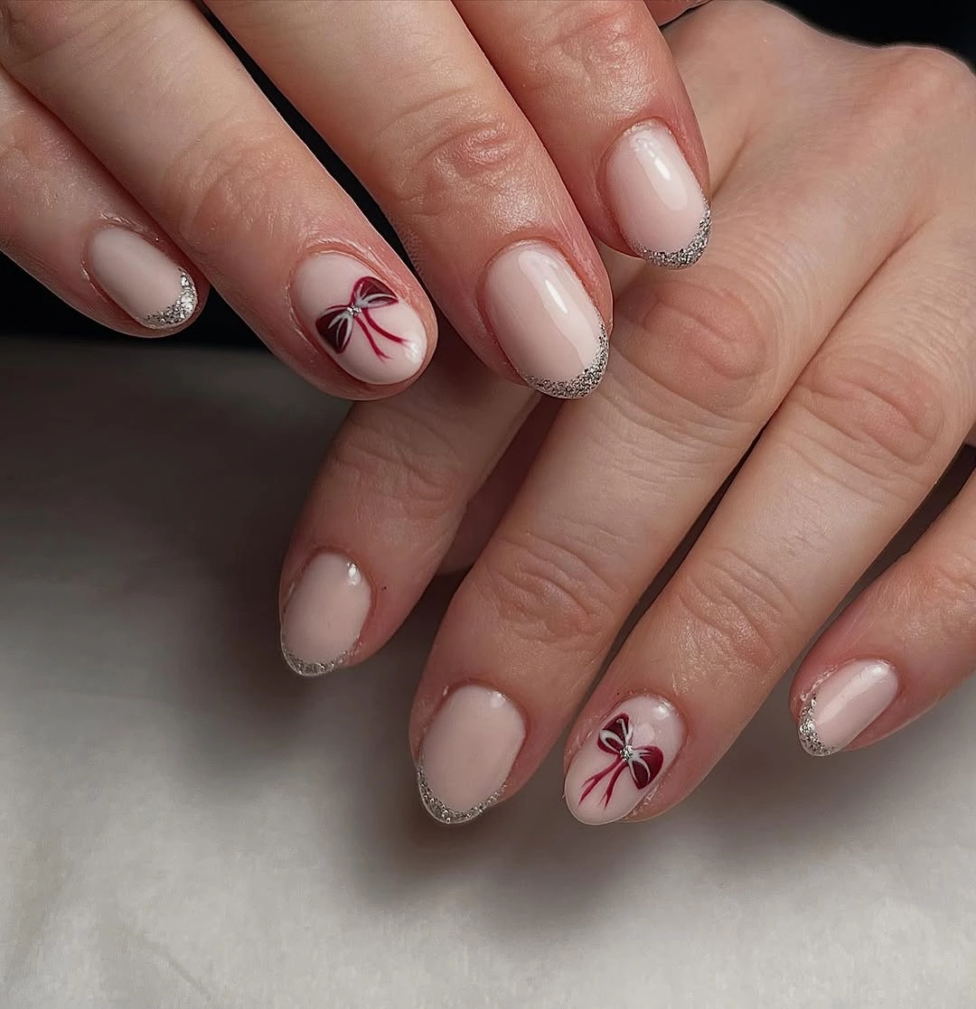 Short rounded milky pink nails with silver glitter tips and burgundy bows