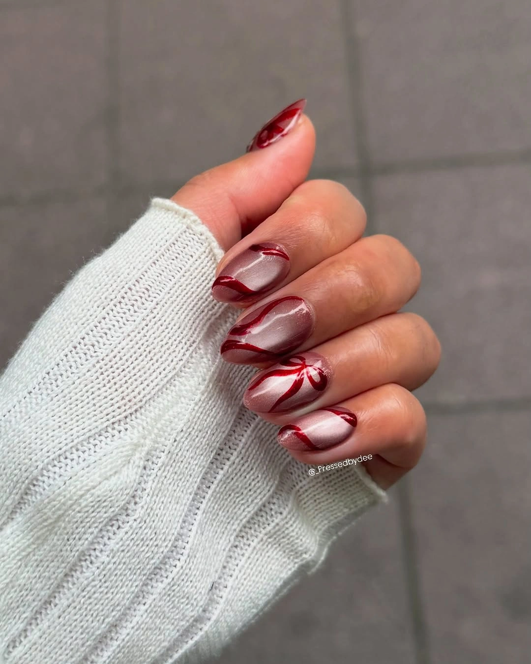 Pearlescent almond nails with curved crimson stripes and a red ribbon bow