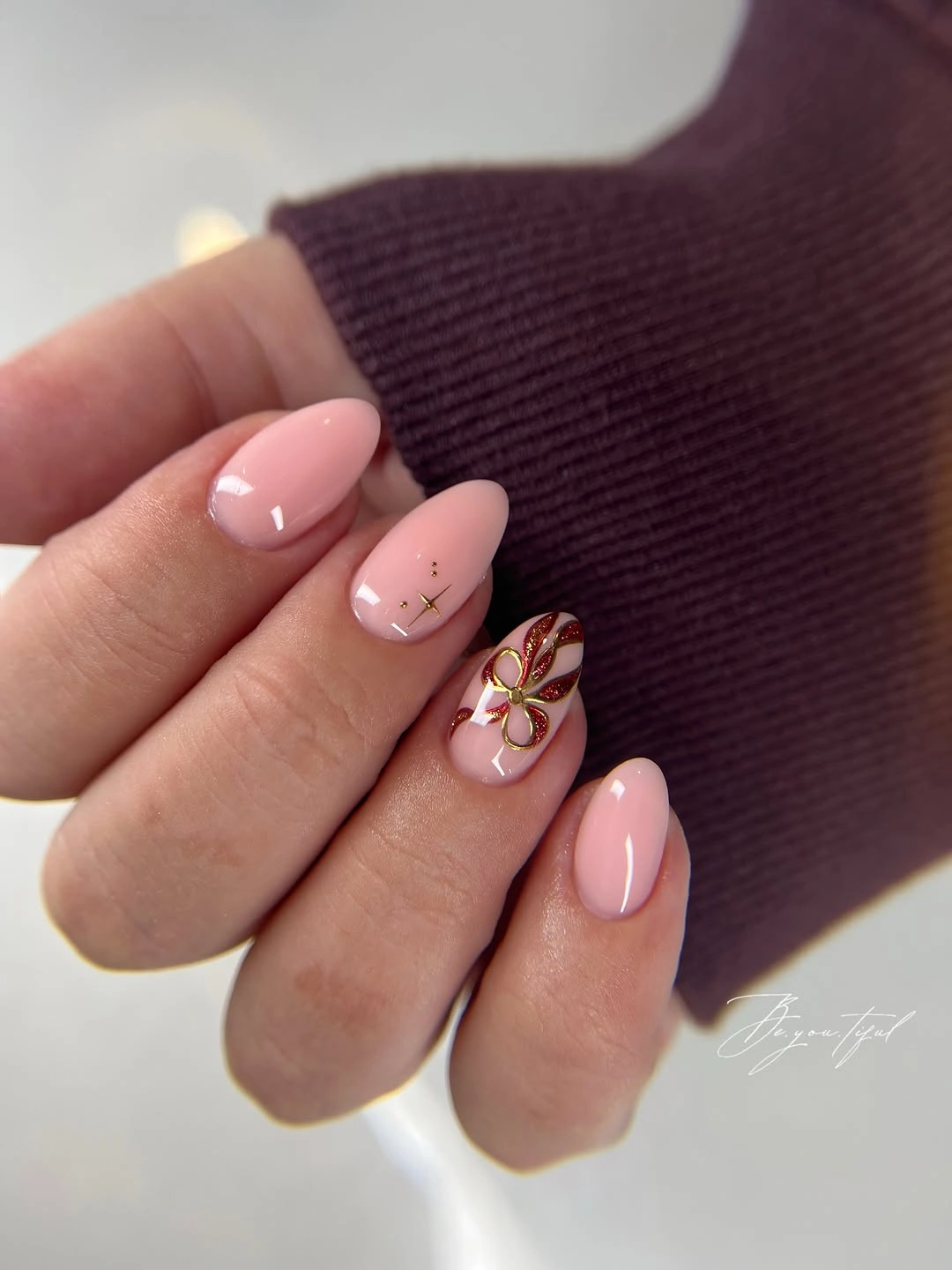 Glossy baby pink oval nails with red gold bow and tiny stars