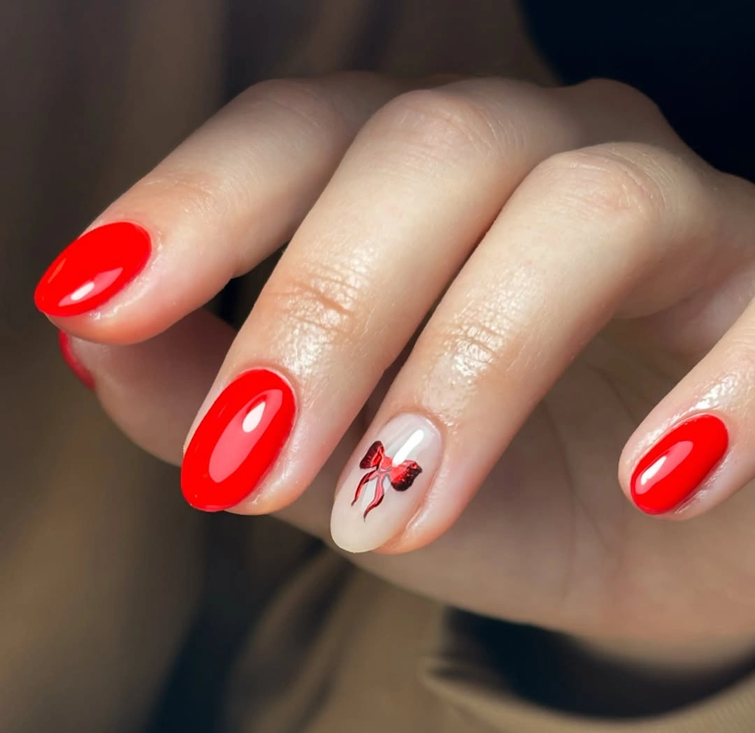 Short glossy scarlet red nails with nude accent and small red bow