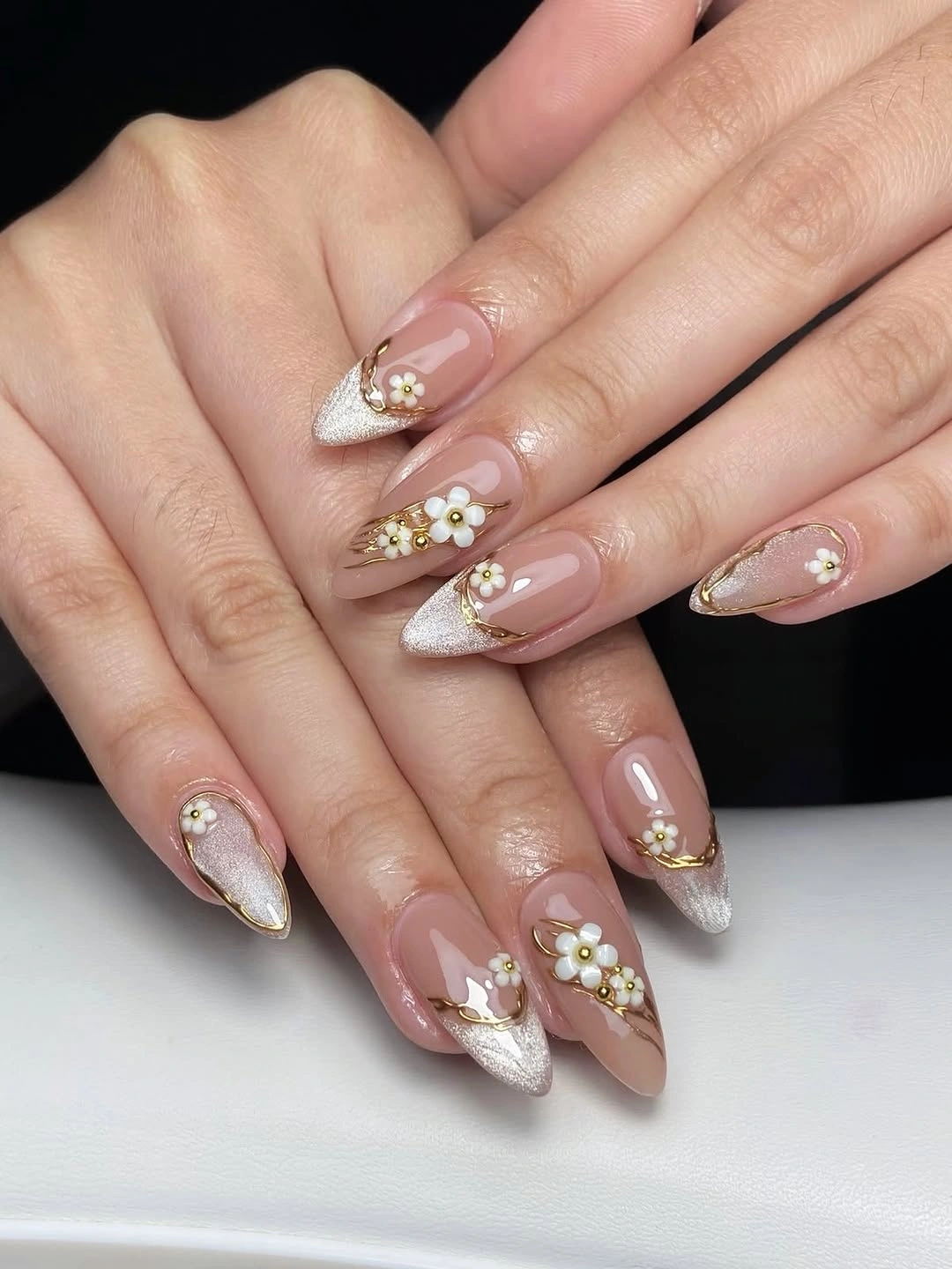 Long almond nails with silver French tips, gold curves, and white flowers