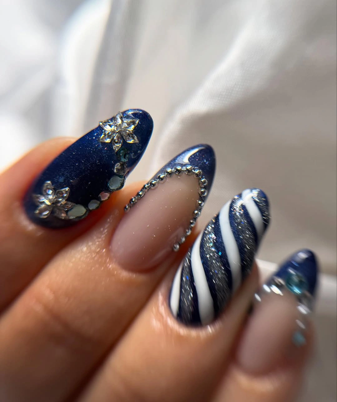 Navy almond nails with silver floral gems, nude sections, and white stripes