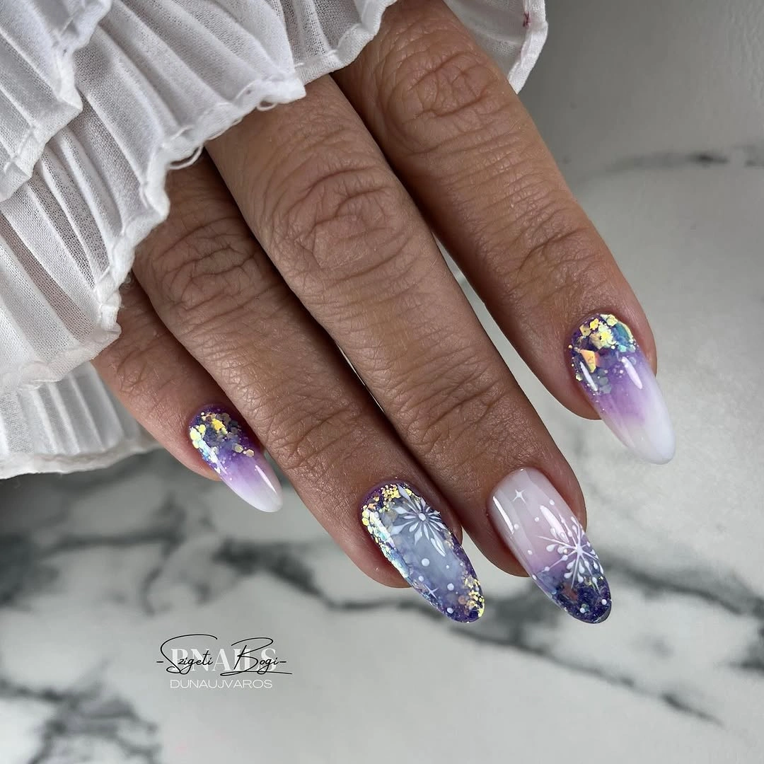 Long almond nails with lilac gradients, white snowflakes, and reflective gold flakes