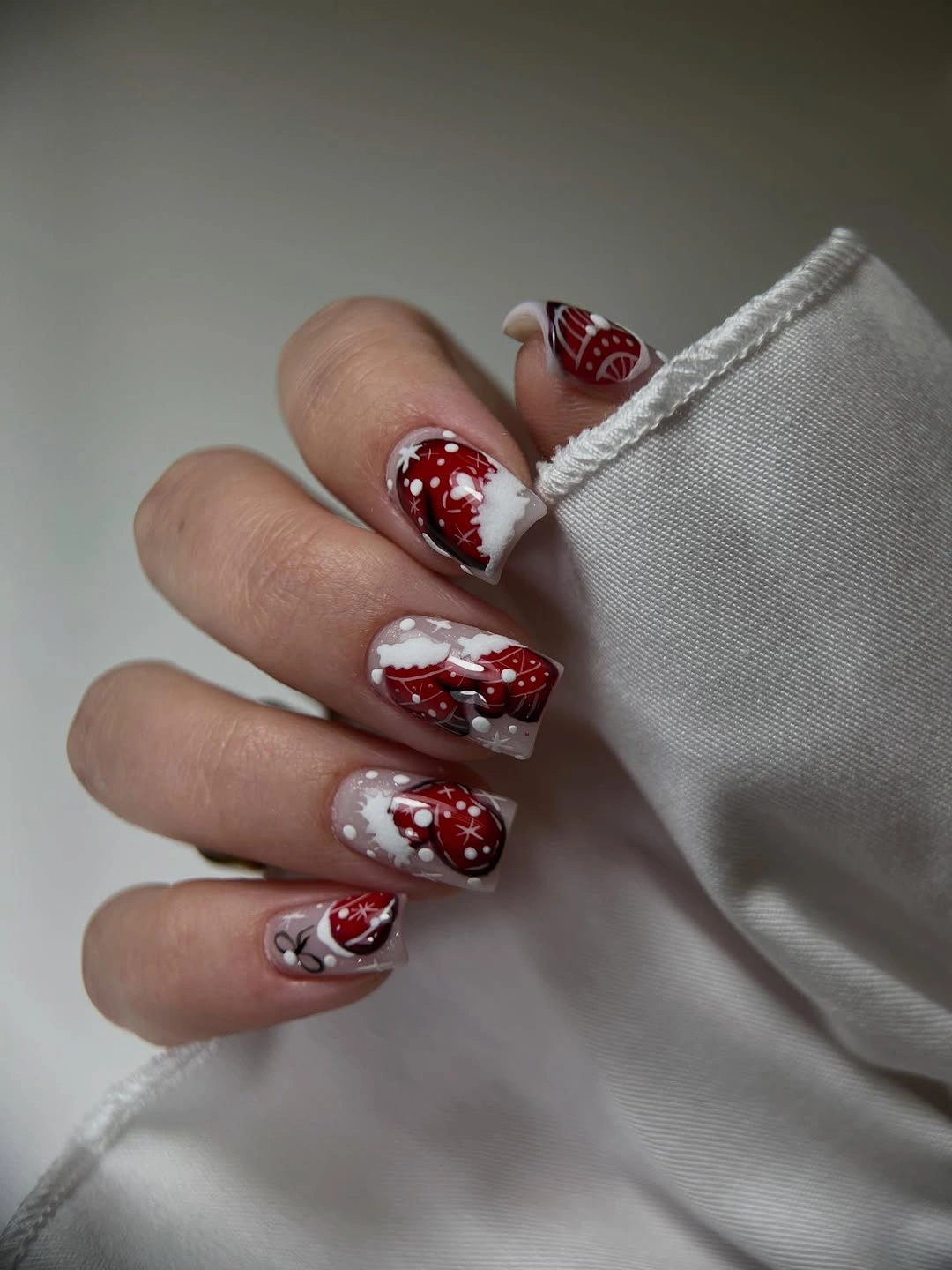 Square nails with red holiday illustrations, white details, and sheer nude backgrounds