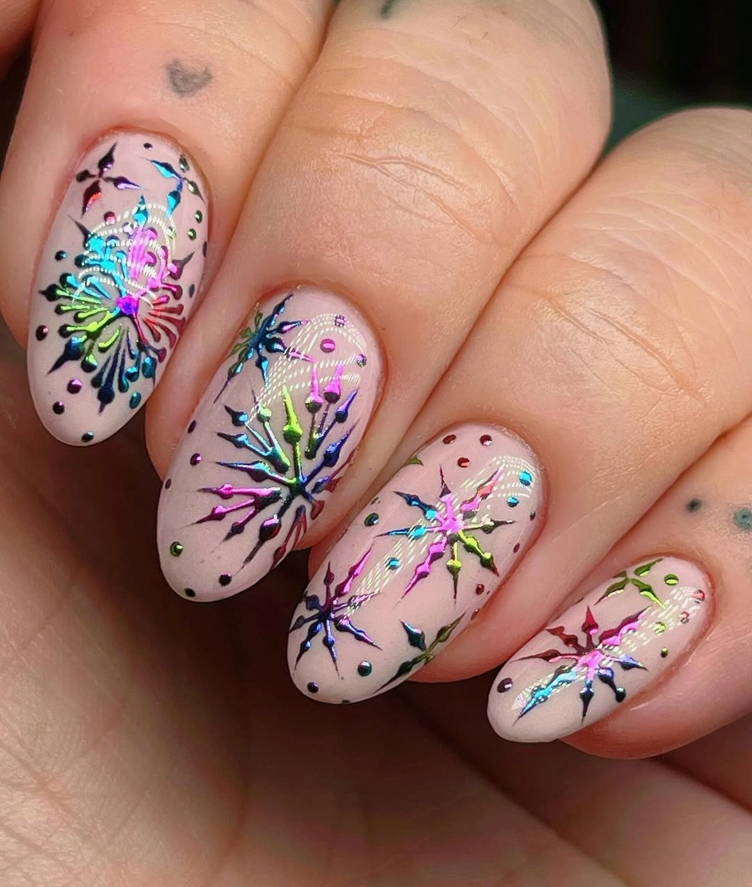 Pink almond nails with multicolored reflective starbursts and scattered decorative dots