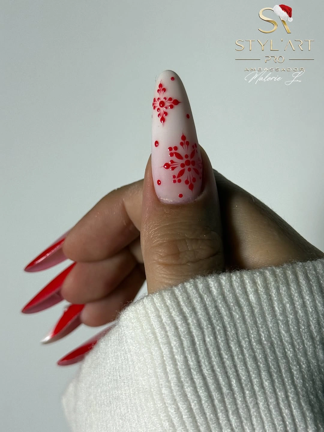 Long pointed pink thumb nail with red snowflake motifs and dots