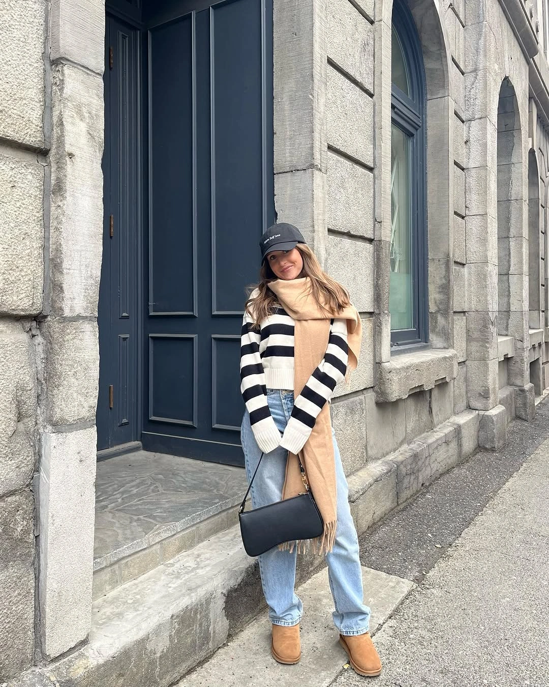 Woman wearing striped sweater, long camel scarf, loose blue jeans and tan boots