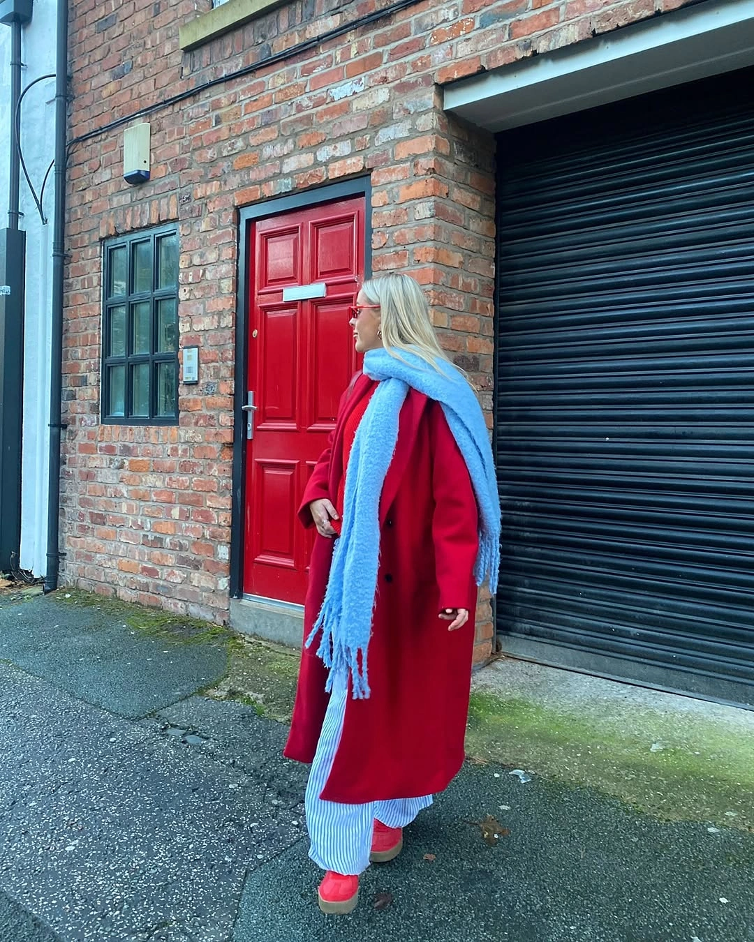 Woman in long red coat, bright blue scarf, striped trousers and pink-red shoes