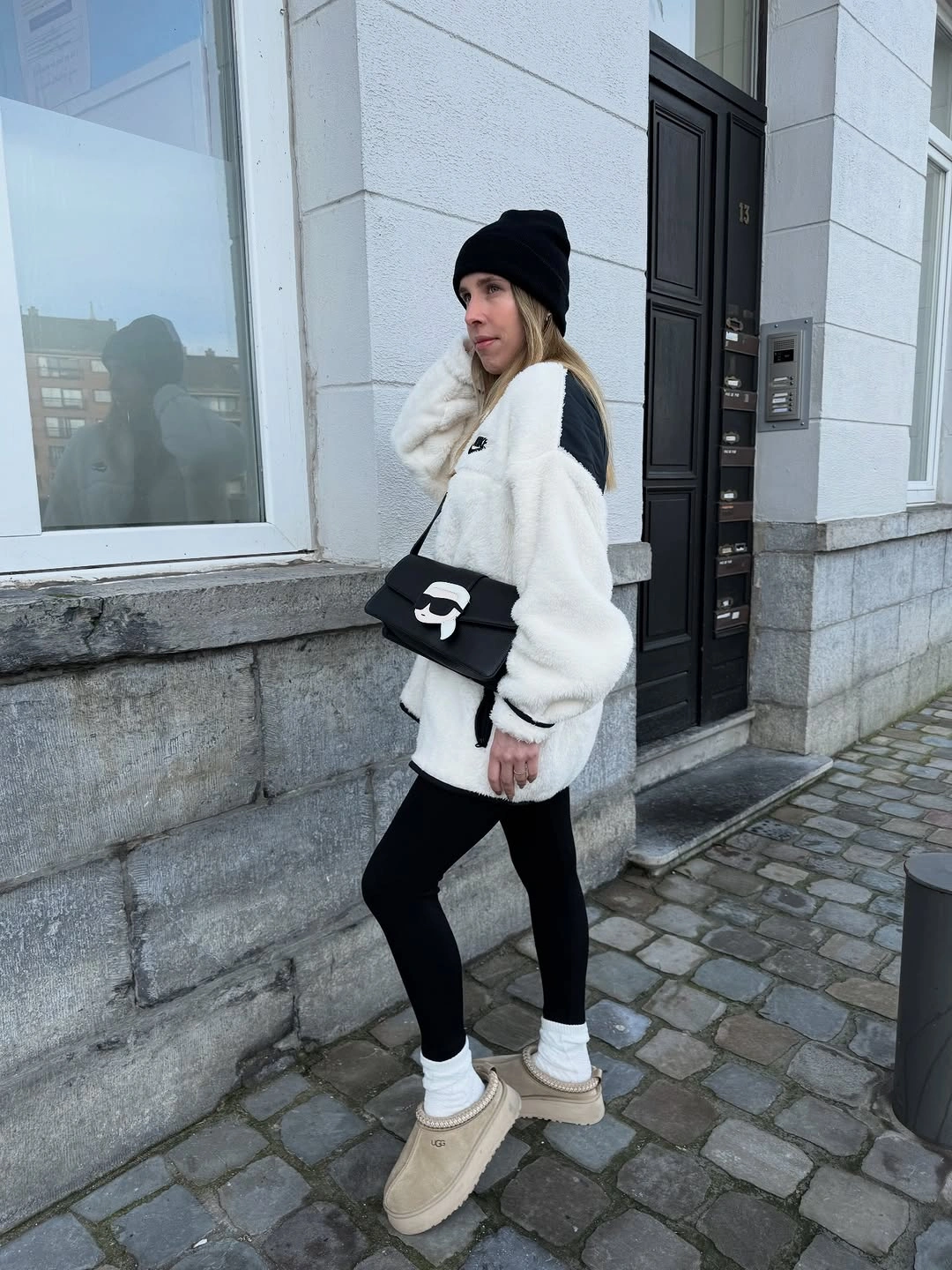 Woman in cream fleece-style pullover, black leggings, beanie and beige slip-ons
