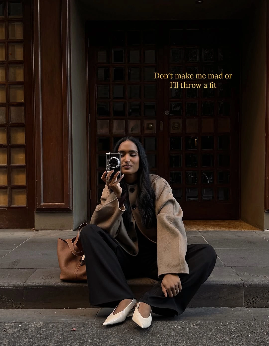 Boxy camel jacket with wide black trousers, cream flats, and tan tote