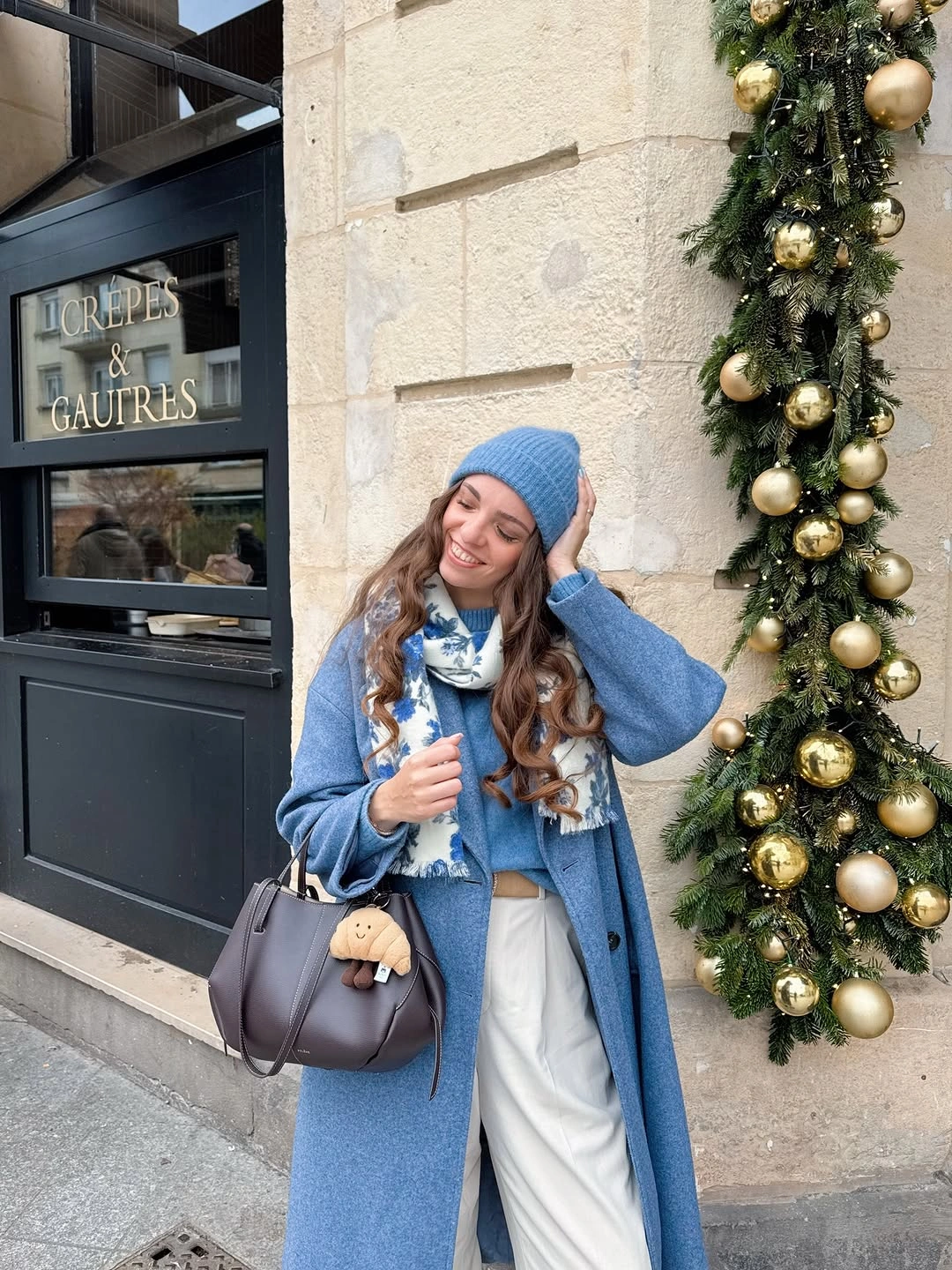 Long blue coat with matching knit hat, patterned scarf, and light trousers